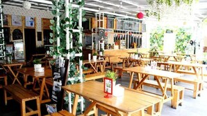 En restaurant med træborde og bænke, en tavle med menuen og grønne planter.