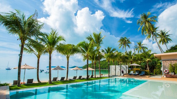 A pool area with lounge chairs and umbrellas, palm trees, and a view of the sea. - Bandara Pool Villas, Phuket (Wichit)