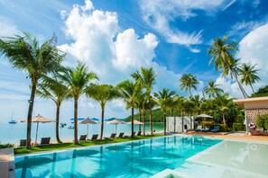 A pool area with lounge chairs and umbrellas, palm trees, and a view of the sea. - Bandara Pool Villas, Phuket (Wichit)