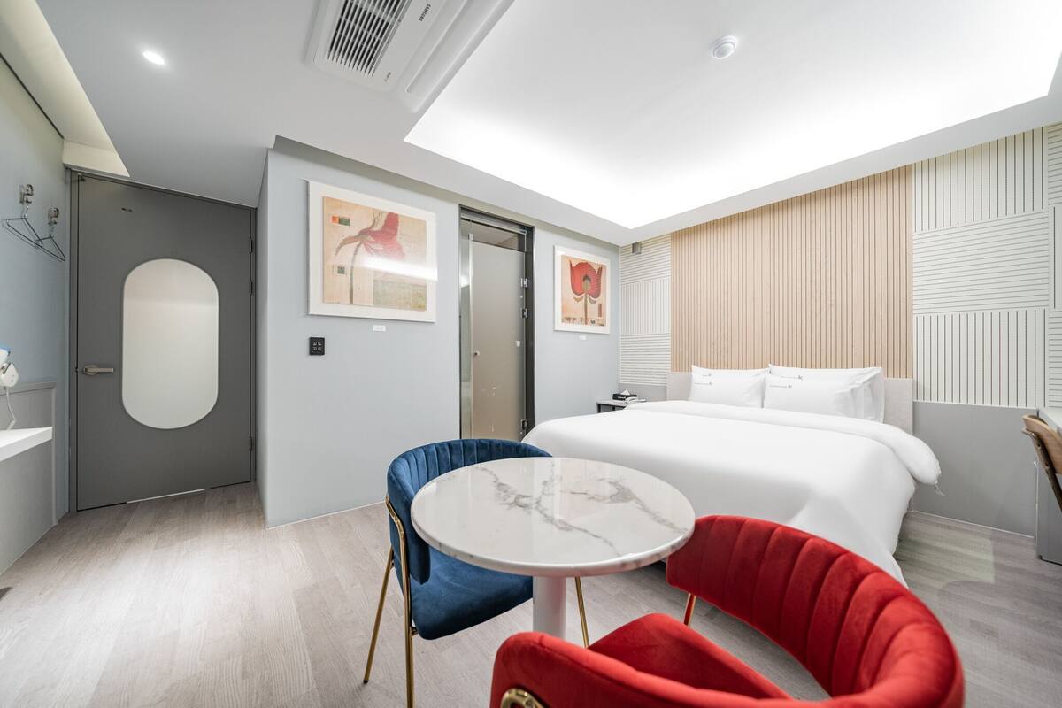 Una moderna camera d'albergo con un letto, un tavolo rotondo, due sedie, un armadio e una porta.
