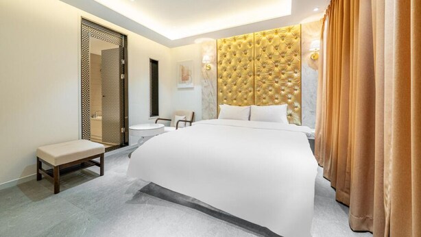 Una habitación de hotel moderna con una cama grande, un banco, una mesita y un baño con puerta estampada.
