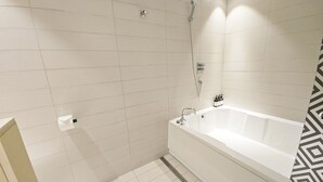 Un baño con paredes de azulejos blancos, una bañera blanca y un cabezal de ducha.