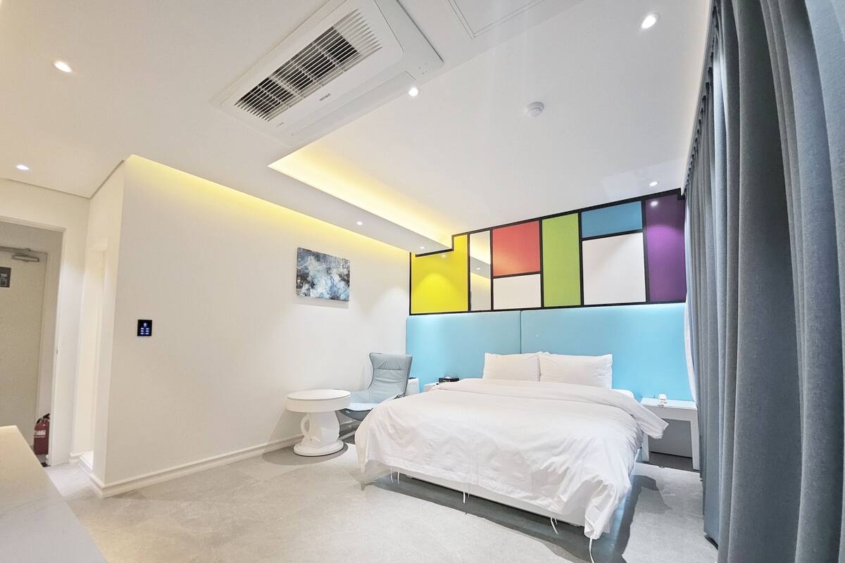 Camera d'albergo moderna con un letto, comodino e un'opera d'arte astratta dai colori vivaci appesa al muro.