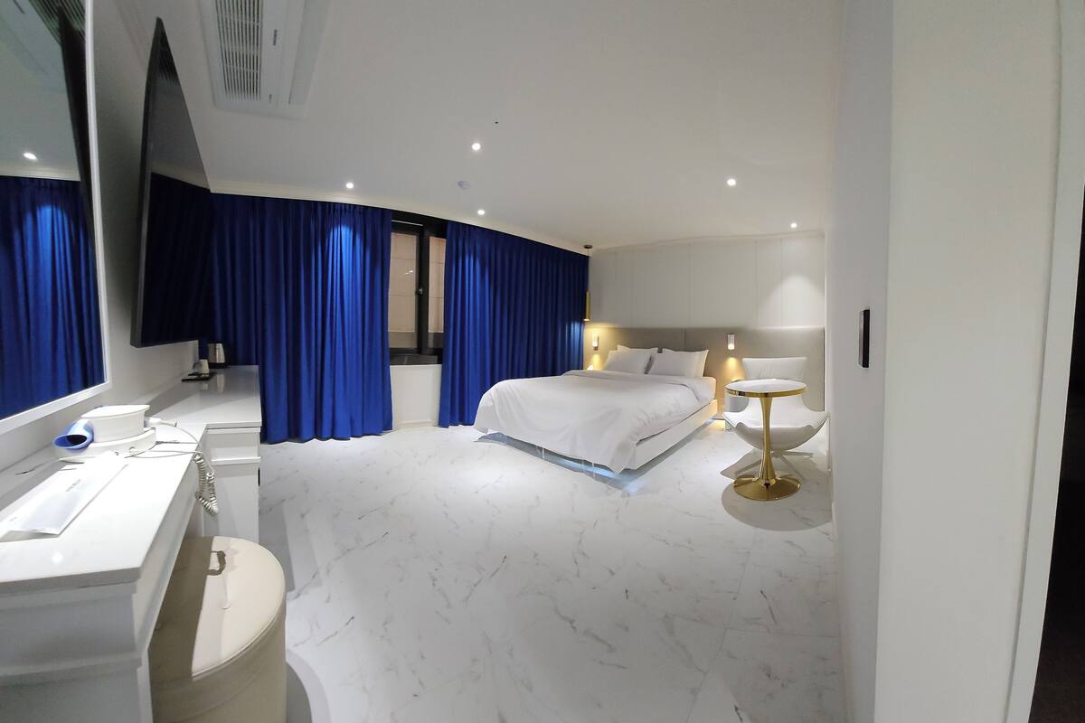 Una moderna camera d'albergo con un letto grande, un comodino, una scrivania con una sedia, uno specchio e un bagno con il water e il lavandino.