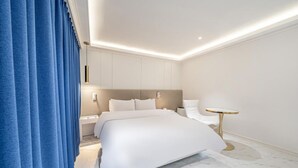 Habitación de hotel moderna con una cama grande, una mesita de noche, una mesa redonda y una cortina azul.