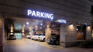 Eine Hotelgarage mit mehreren parkenden Autos und einer Neonreklame, die den Parkbereich kennzeichnet.