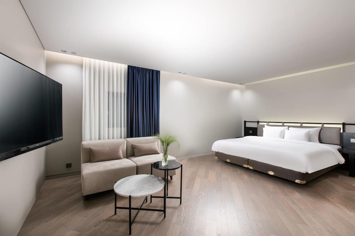 Una habitación de hotel moderna con una cama grande, un sofá, una mesita y un televisor.