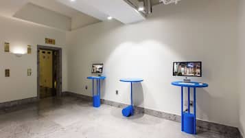 Un corridoio moderno con pavimento in marmo, tavolini decorati in blu e un display digitale sulla parete.
