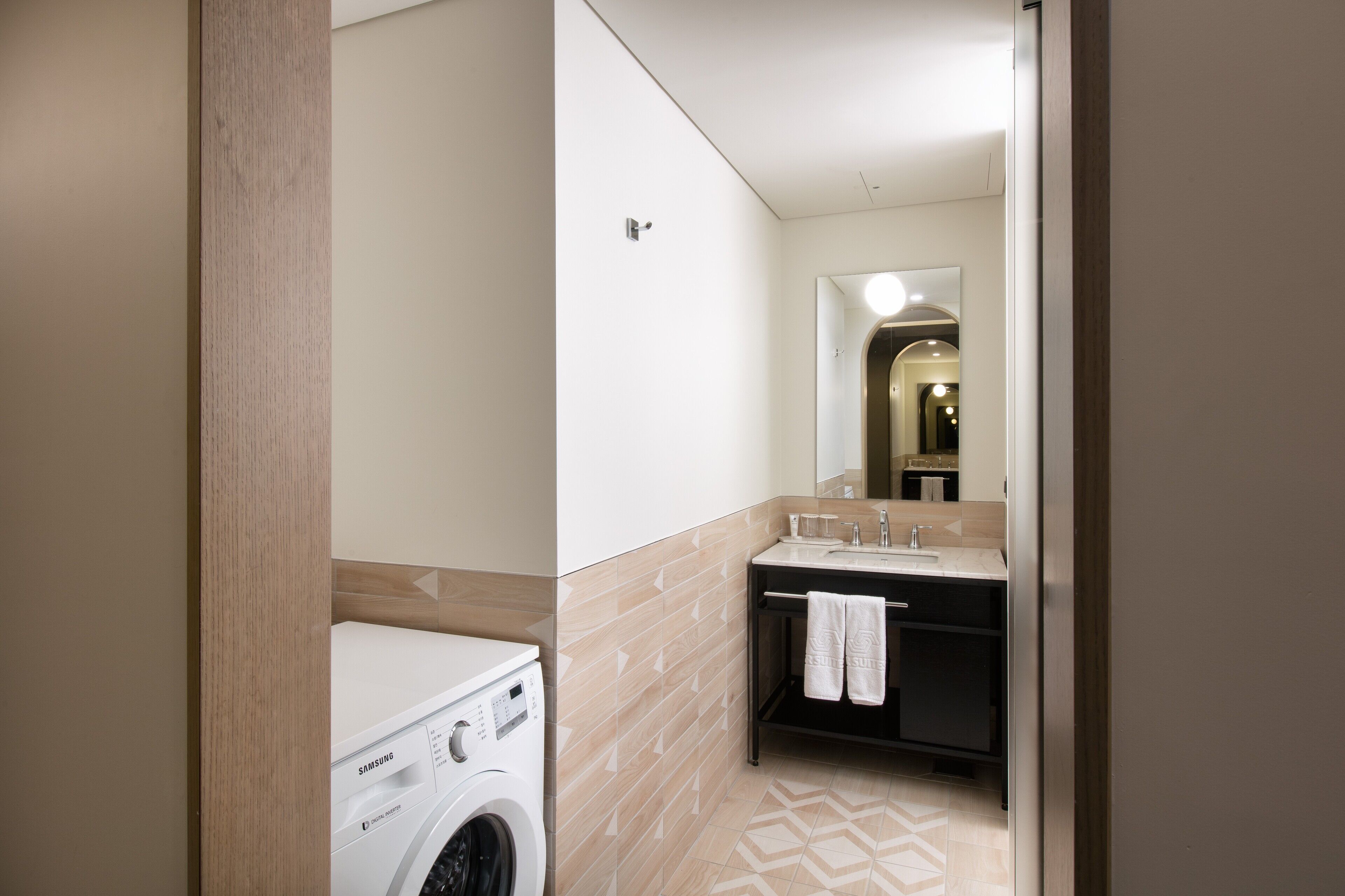 A compact bathroom with a washing machine, a sink, and a towel rack.