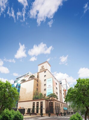A hotel with a prominent sign, a parking area, and a clear blue sky with clouds. - SR Suites Pangyo (Seongnam)