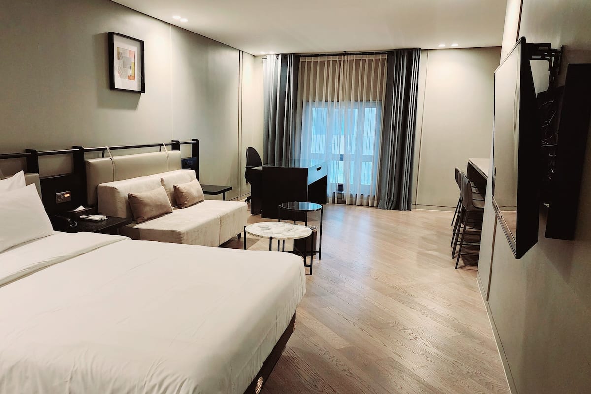 Habitación de hotel con dos camas, un escritorio, una silla, una mesita y un televisor.