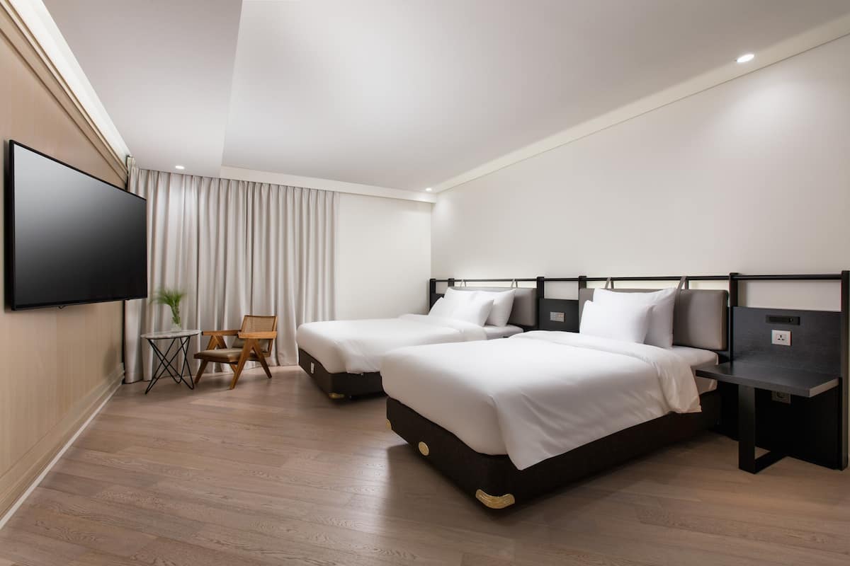 Una habitación de hotel moderna con dos camas, un televisor de pantalla plana, una mesita pequeña y una silla.