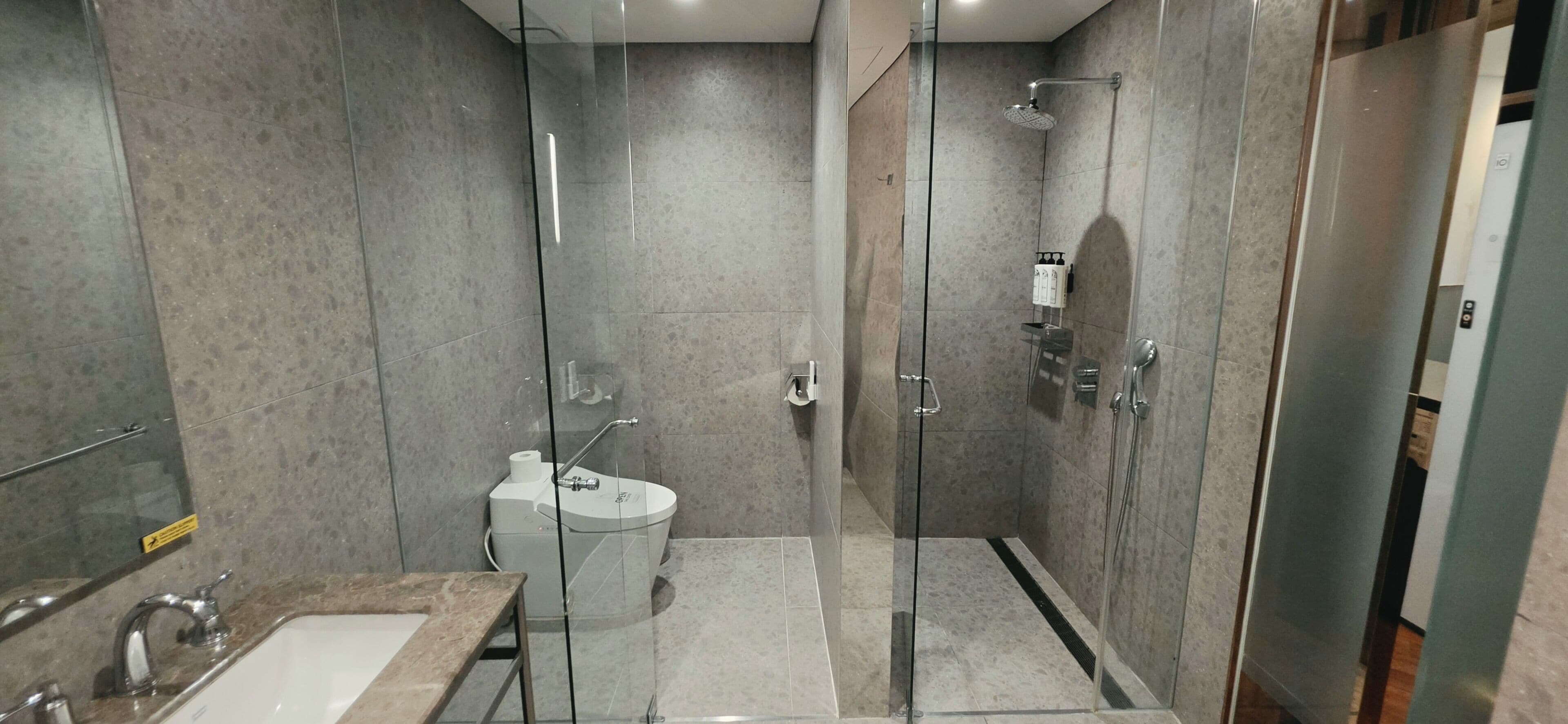 Un baño moderno con ducha envuelta en vidrio, inodoro y lavamanos con encimera de mármol.