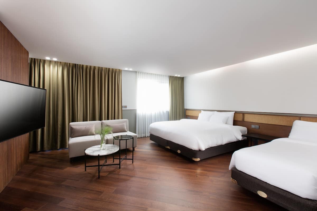 Una habitación de hotel moderna con televisión de pantalla plana, un sofá, dos camas y una mesita con un florero.