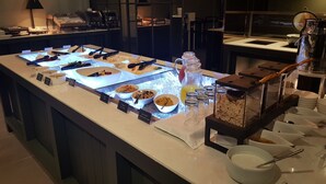 Un bufé con diversas opciones de comida, incluyendo ensaladas y otros platos, dispuestos en un mostrador con vitrina de cristal.