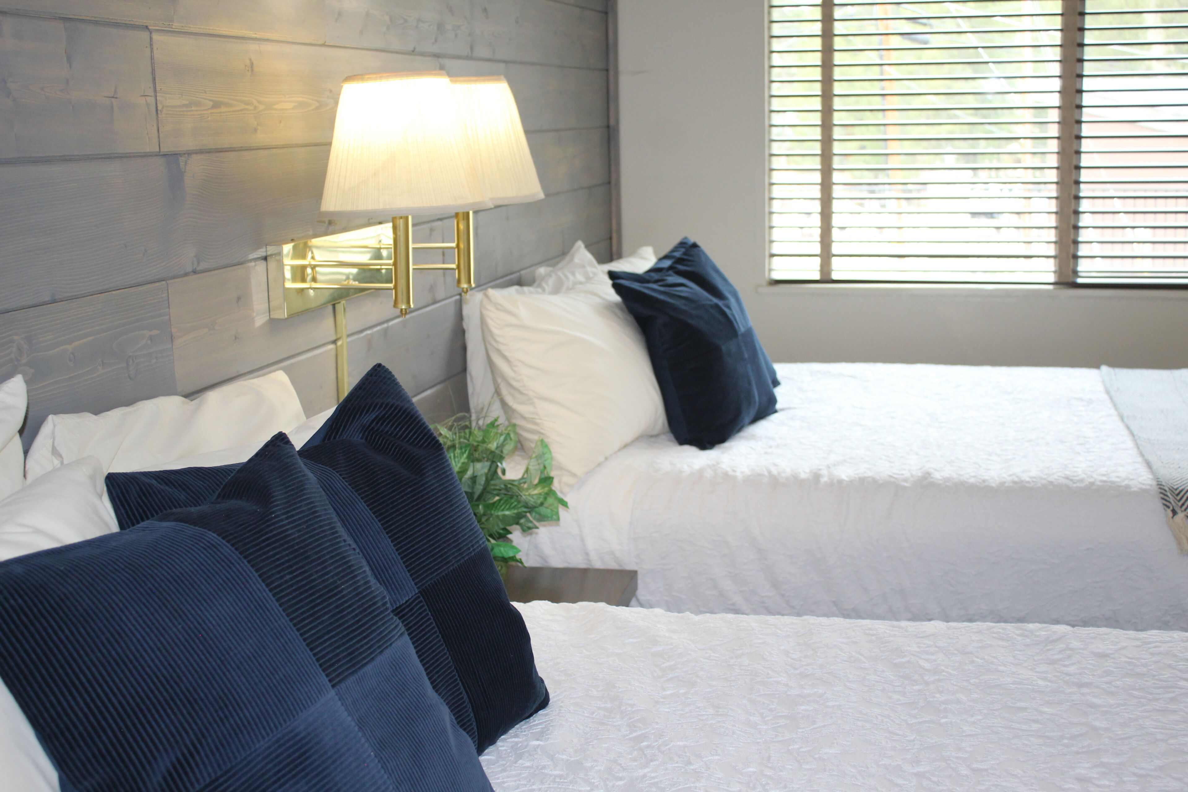 Une chambre d’hôtel avec deux lits, une lampe et une fenêtre avec des stores.