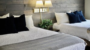 Ein Hotelzimmer mit zwei Betten, einem Holz-Kopfteil, einer Wandlampe und einem Blumentopf.