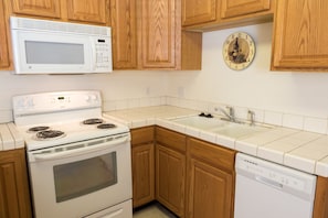 A kitchen with wooden cabinets, a white stove, a microwave, a sink, and a clock. - Whispering Pines (June Lake)