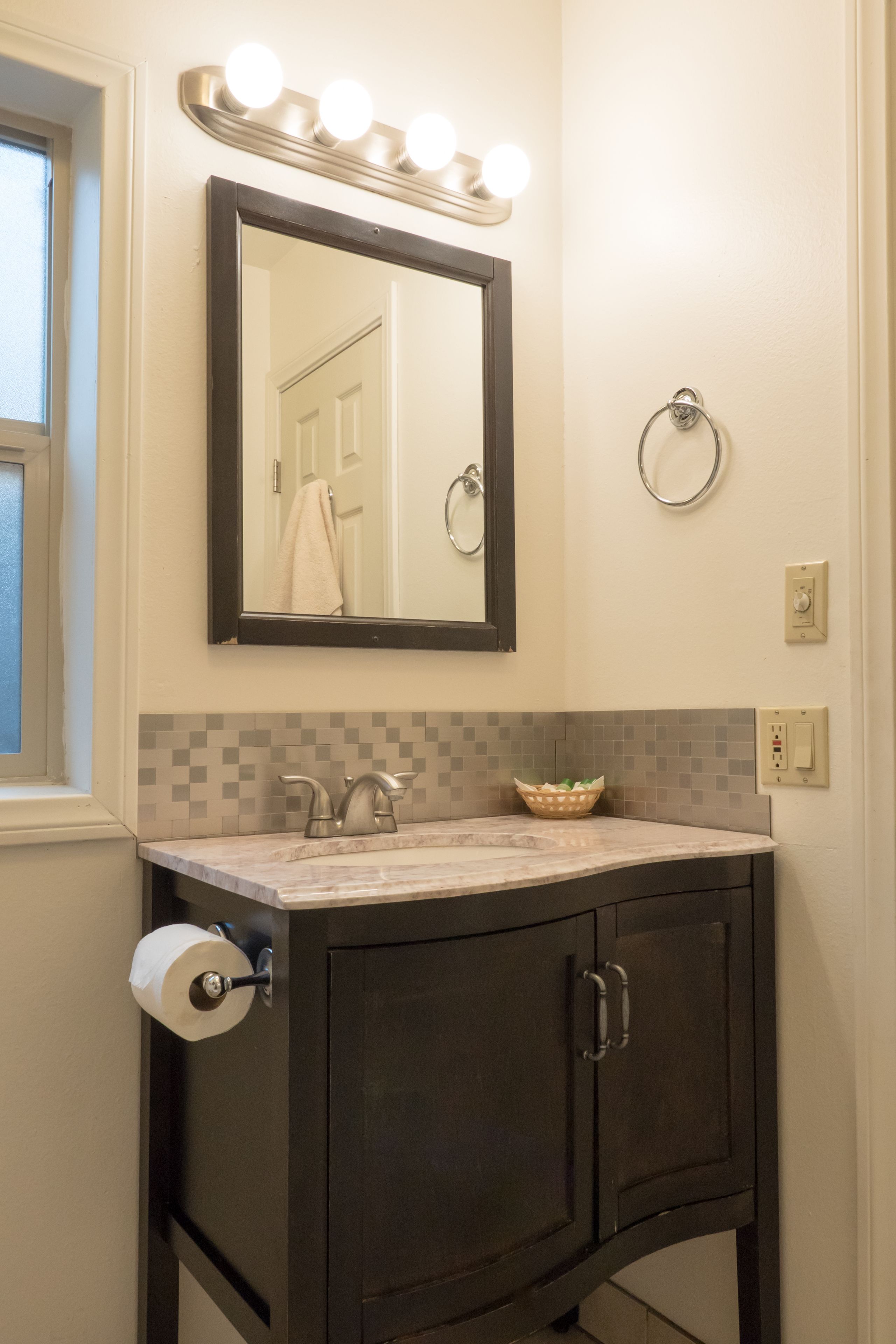 A bathroom with a vanity, a mirror with lights, a towel ring, and a toilet paper holder.