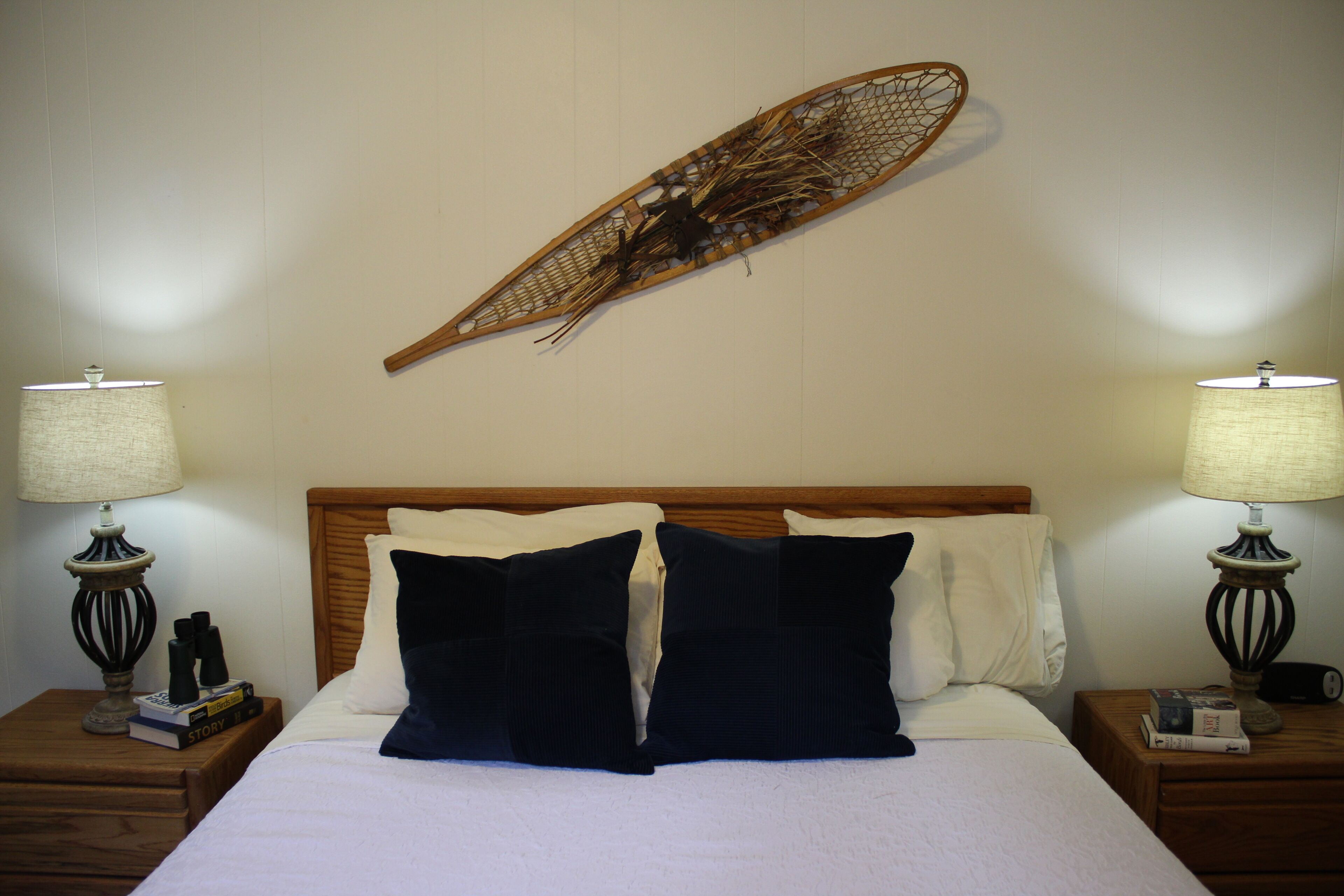 A neatly made bed with a wooden headboard, two bedside tables with lamps, and a wall-mounted decorative piece.