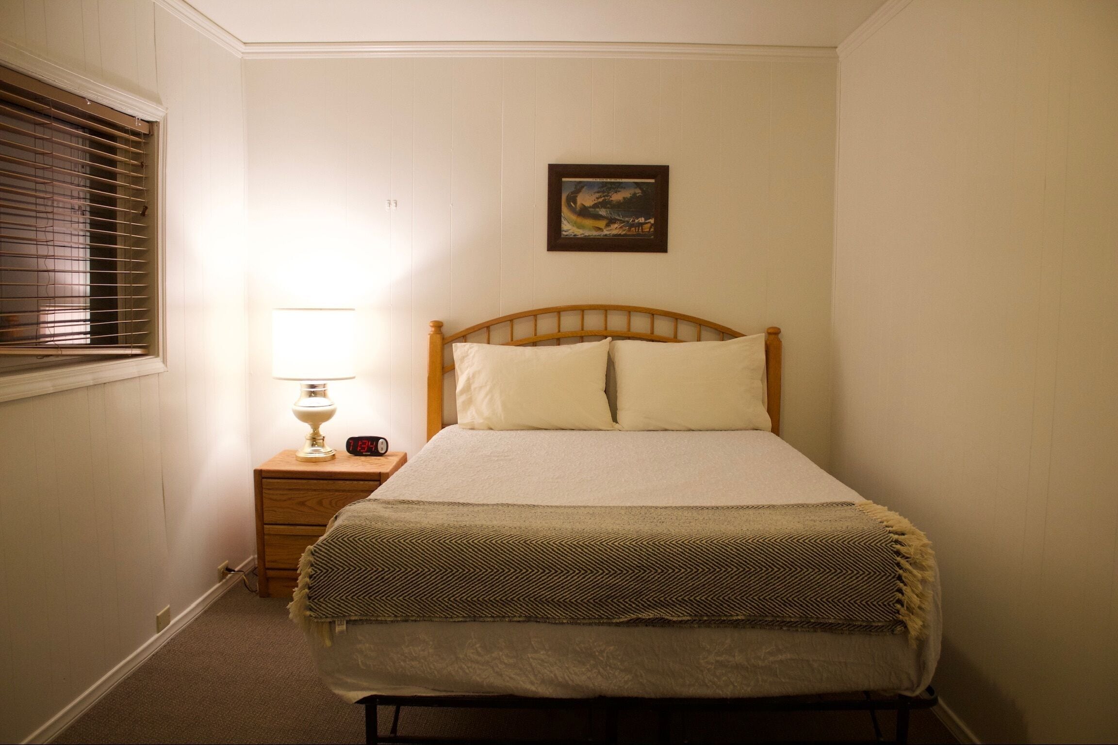 Un dormitorio con una cama, una mesita de noche, una lámpara, un reloj y un cuadro en la pared.
