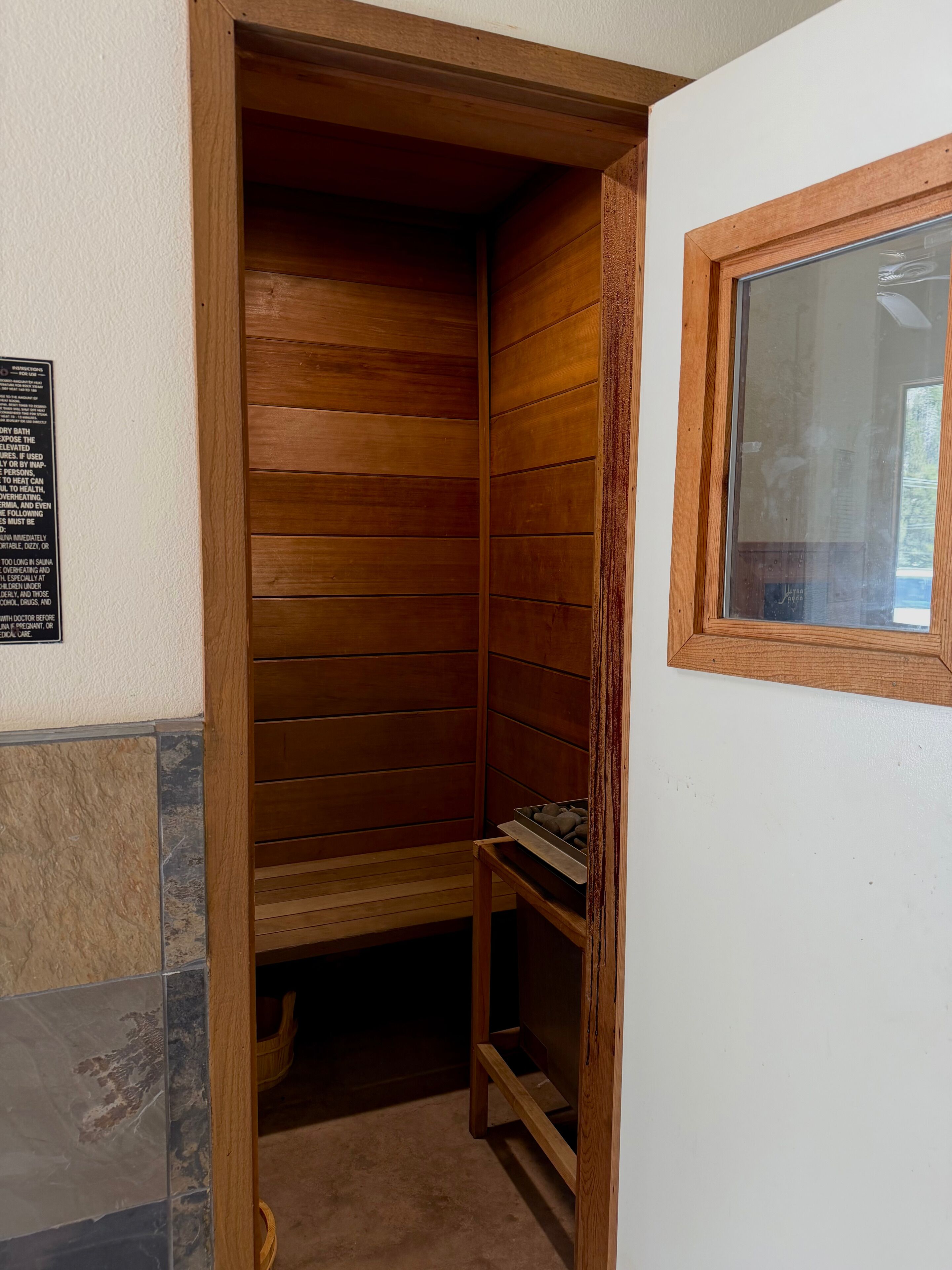 Una sauna de madera con un banco, un estante con objetos y una ventana.