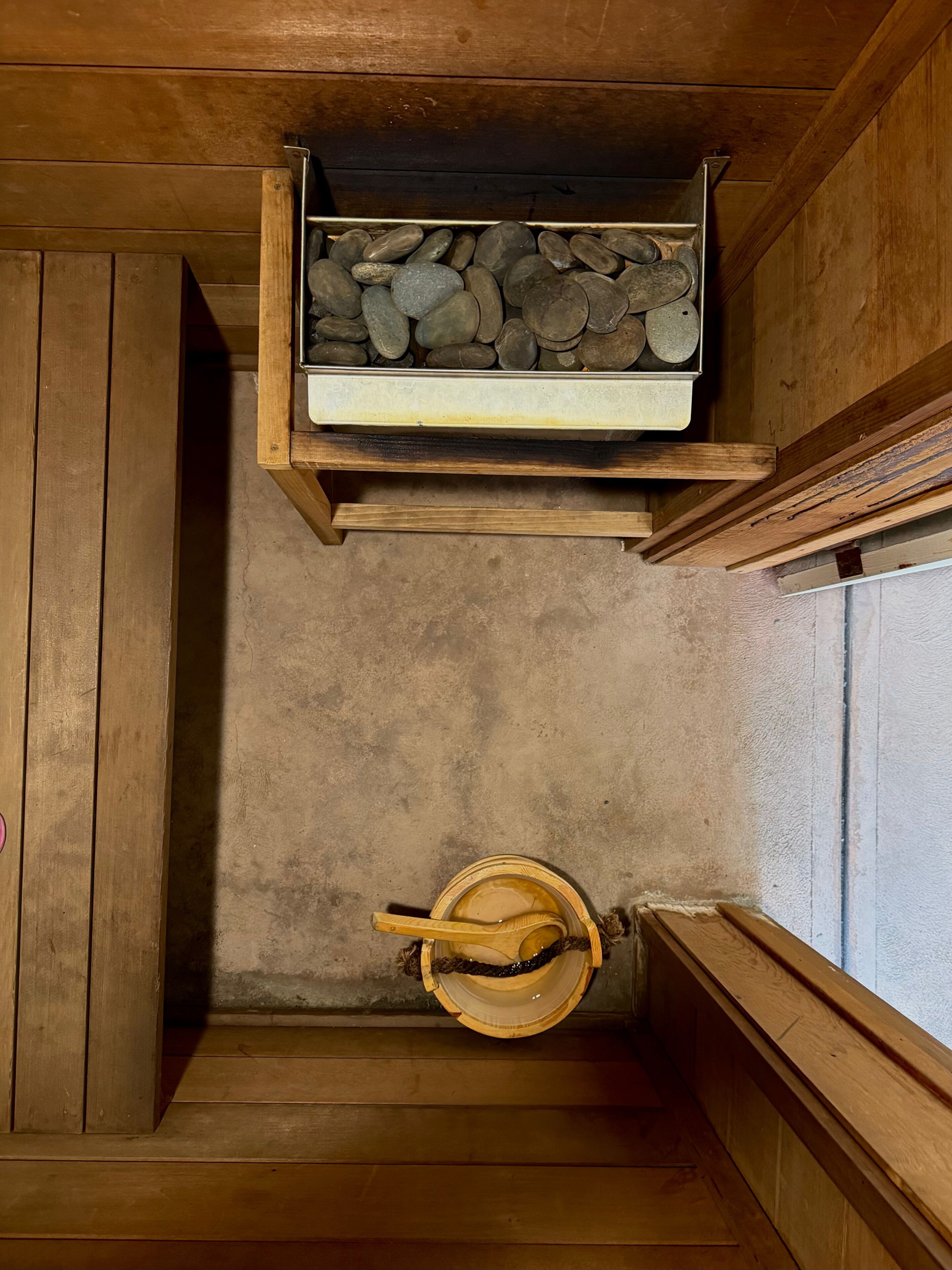 A wooden interior with a stone shelf, a wooden bucket, and a concrete floor.