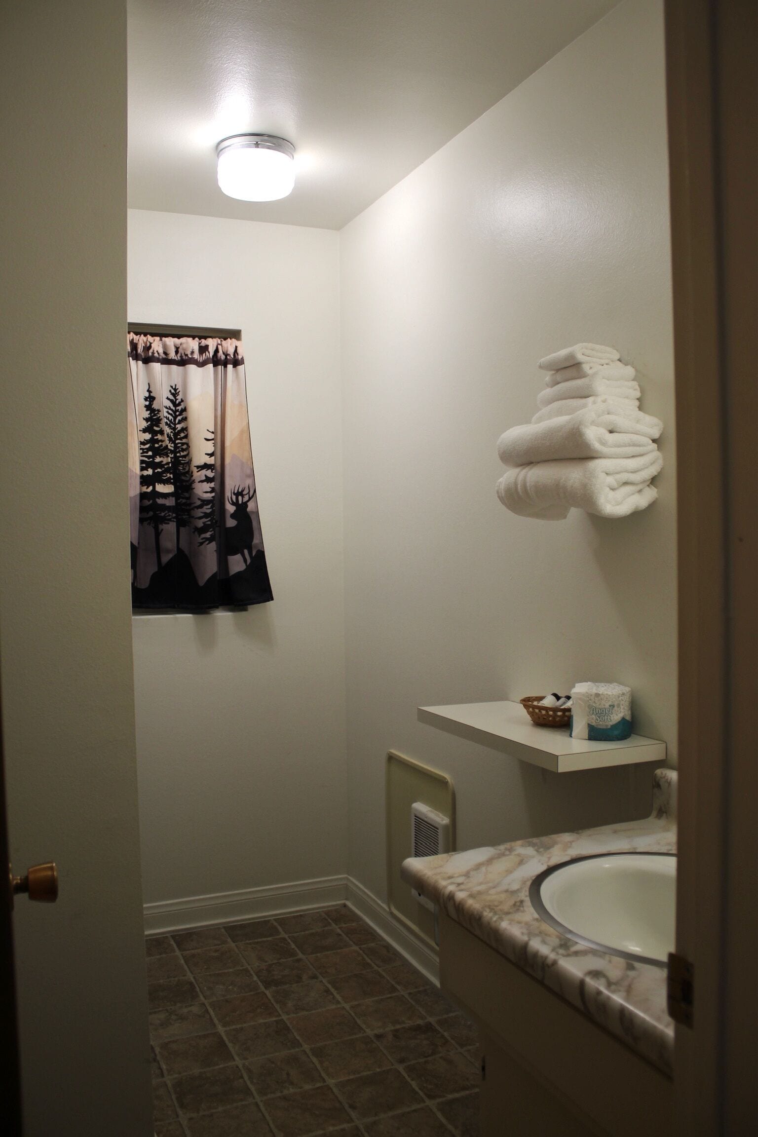 A bathroom with a sink, towel rack, and a window with a forest-themed curtain.