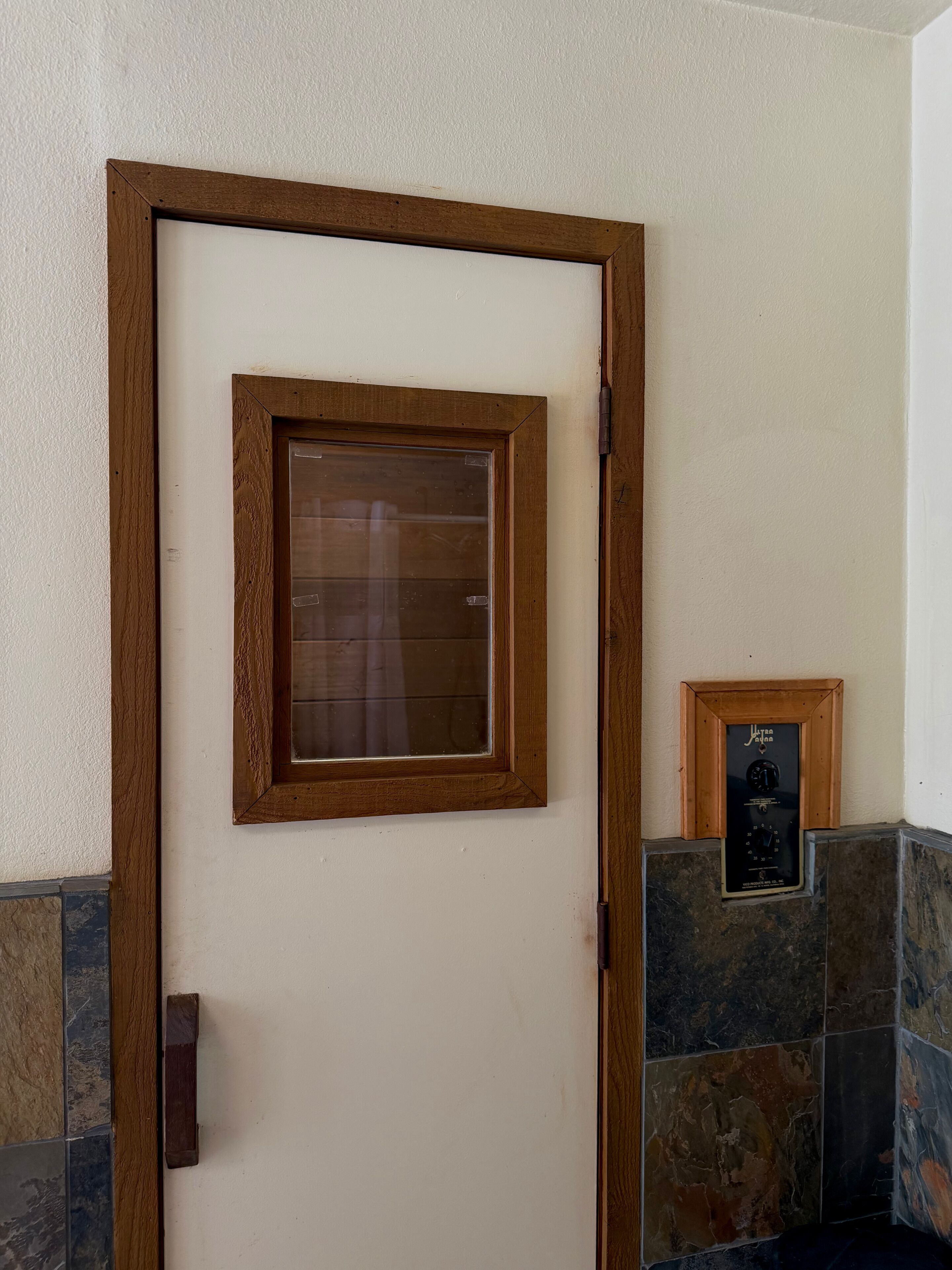 A wooden-framed door with a glass panel, a small plaque, and a stone-tiled wall.