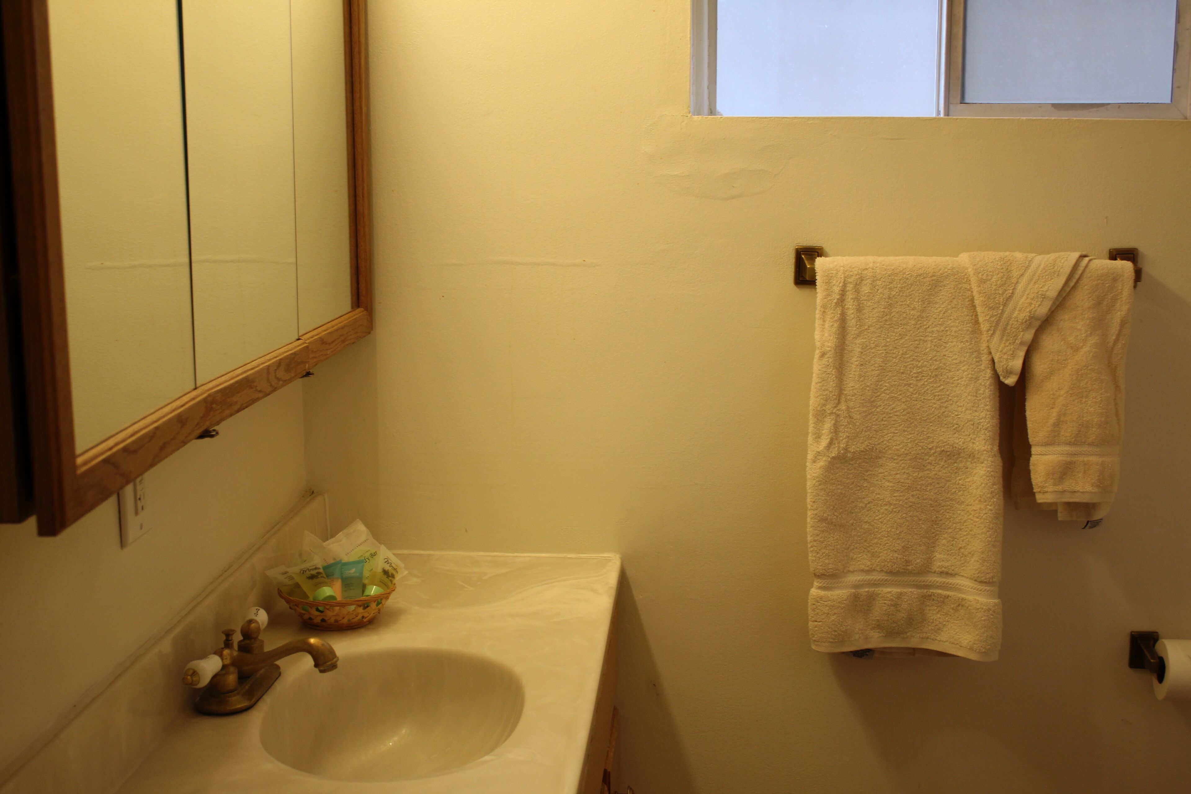 A bathroom with a sink, mirror, towel rack, and a window.