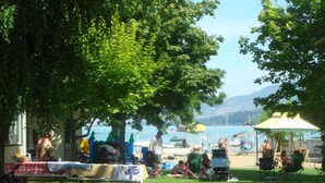 A grassy outdoor area with picnic tables, a covered seating area, and a view of the water. - Kokanee Beach Resort Motel (Lake Country)