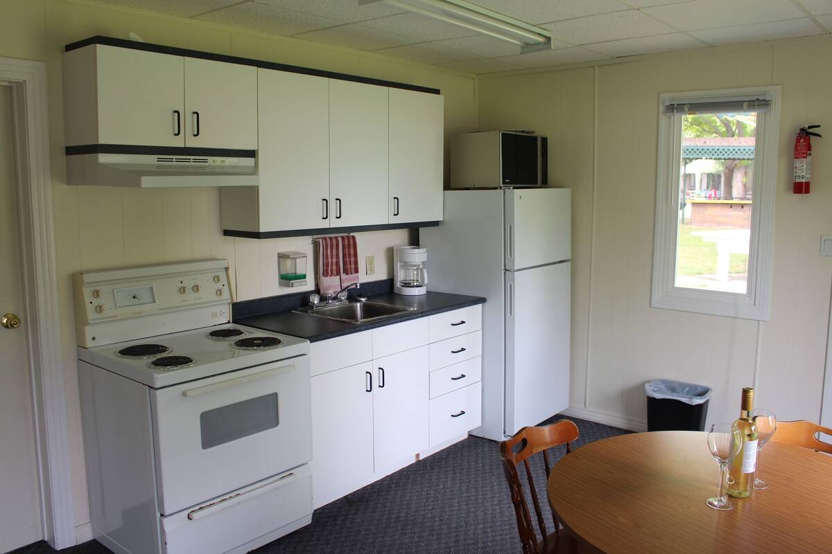 A compact kitchen with white cabinets, a stove, a refrigerator, and a window with a view of the outdoors.