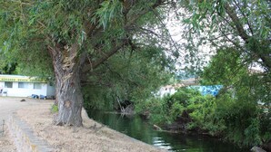 A river with a tree-lined bank, a stone pathway, and a building with a sign reading "KOKANEE BEACH RESORT". - Kokanee Beach Resort Motel (Lake Country)