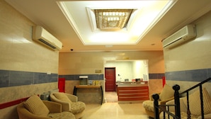 A lobby with a reception desk, two armchairs, a staircase, and a ceiling light fixture. - Al Maha Residence RAK (Ras Al Khaimah)