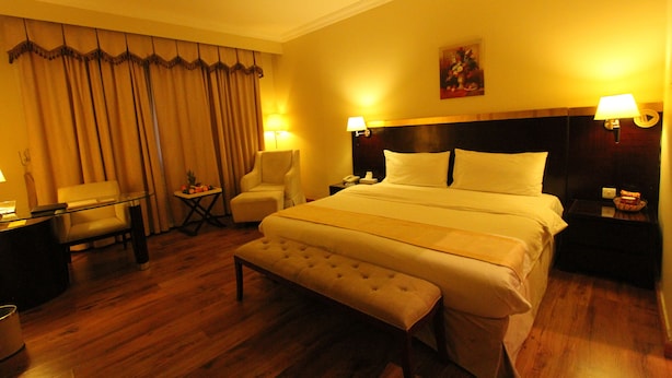 A hotel room with a large bed, two bedside tables with lamps, a small table with a chair, and a bench. - Al Maha Residence RAK (Ras Al Khaimah)