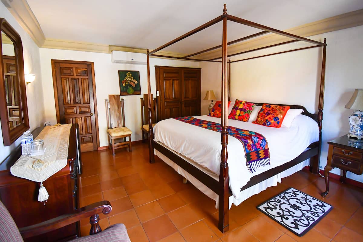 Una cama con dosel con un edredón colorido, muebles de madera y suelo de baldosas.