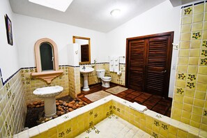 Een badkamer met een wastafel, toilet en douchegedeelte, met betegelde wanden en een houten deur.