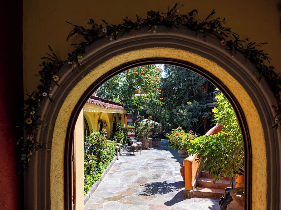 An arched doorway leading to a courtyard with stone flooring, potted plants, and outdoor seating.