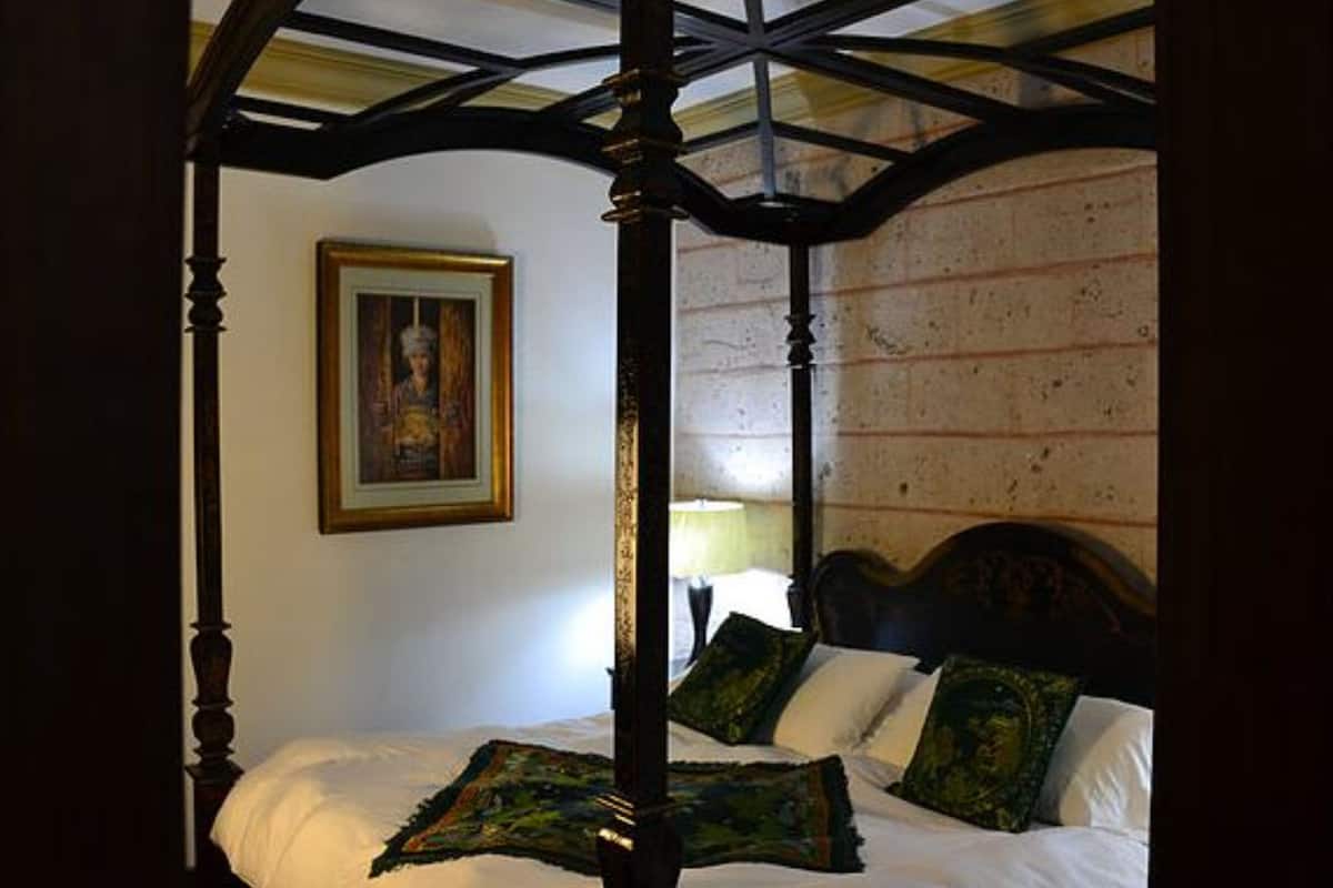 Una cama con dosel y cuatro columnas, cabecera y una lámpara de noche, además de un cuadro en la pared.