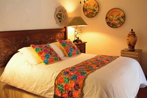Een netjes opgemaakt bed met bloemenbedrukking, een houten hoofdbord en een nachtkastje met een lamp en een vaas.