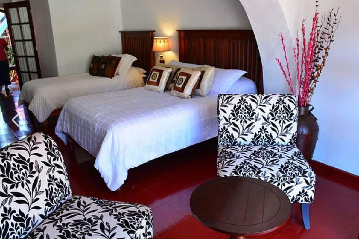 Habitación de hotel con dos camas, zona de estar con una mesa y un jarrón decorativo con ramas.