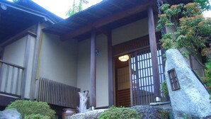 Een traditionele Japanse woning met een houten poort, stenen trappen en een grote rots.