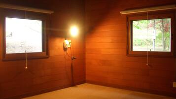 A room with wooden walls, two windows with blinds, a light fixture on the wall, and a carpeted floor.
