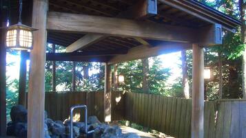A covered outdoor area with a wooden structure, stone seating, and hanging lanterns.