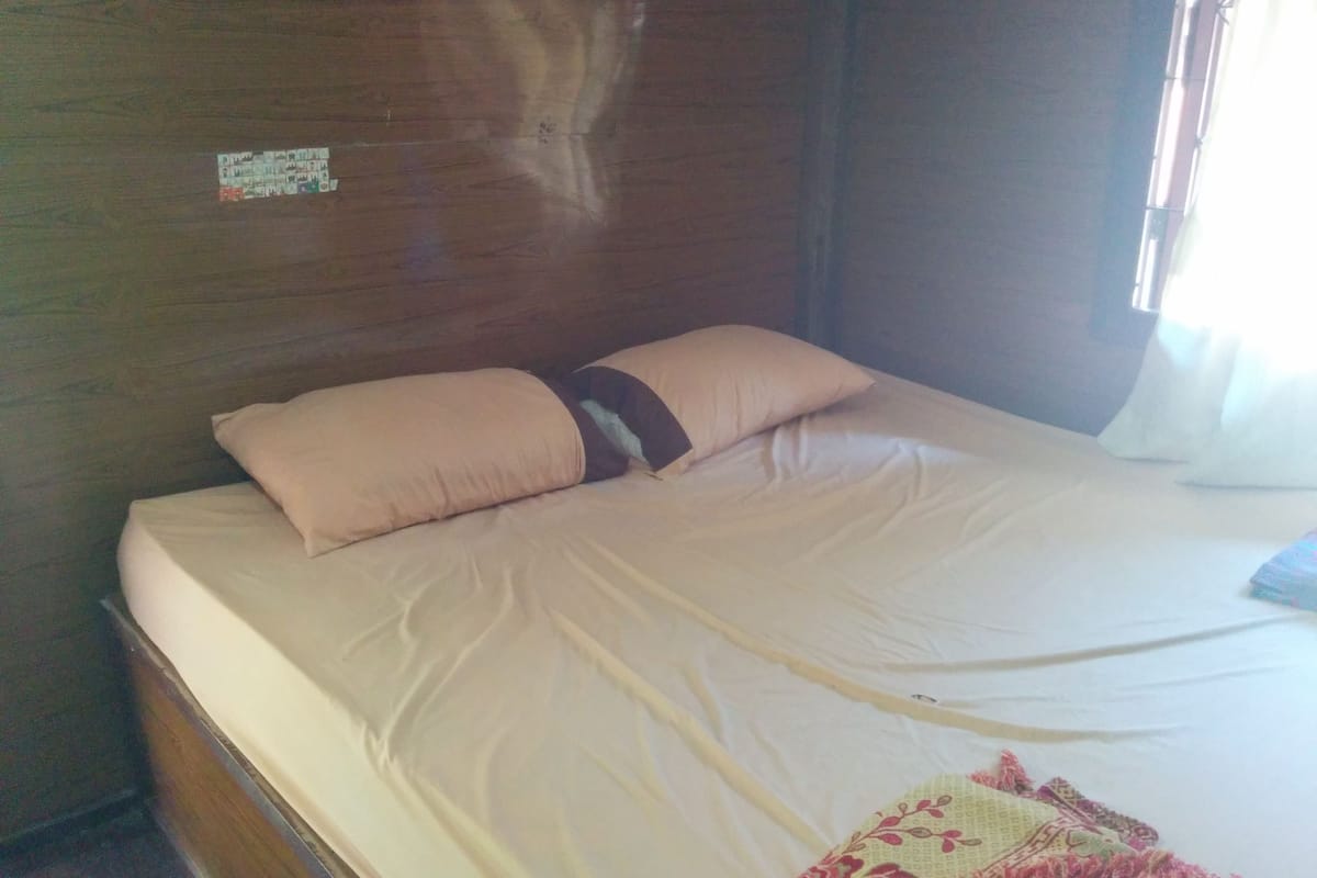 Ein Einzelbett mit einer beigen Matratze und einem Kissen in einem Zimmer mit Holzwänden.