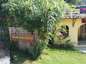 Segnaletica in legno per Paradise Garden Resort, con recinzione rustica e vegetazione lussureggiante.