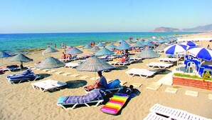 Une plage dotée de nombreuses chaises longues et de parasols, dont certains arborent des marques bien visibles.