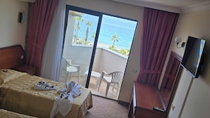 A hotel room with two beds, a TV, a desk, and a balcony with a view of the ocean. - Sunshine Hotel (Alanya)
