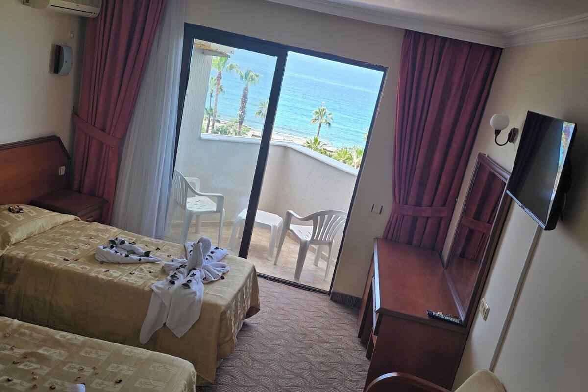 Habitación de hotel con dos camas, televisión, escritorio y balcón con vista al océano.