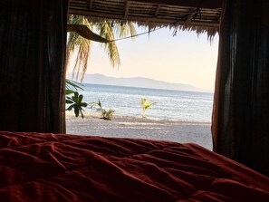 A bed with a red cover, a view of a beach with palm trees, and a thatched roof structure. - Papillon Bungalows (Ko Pha-ngan)